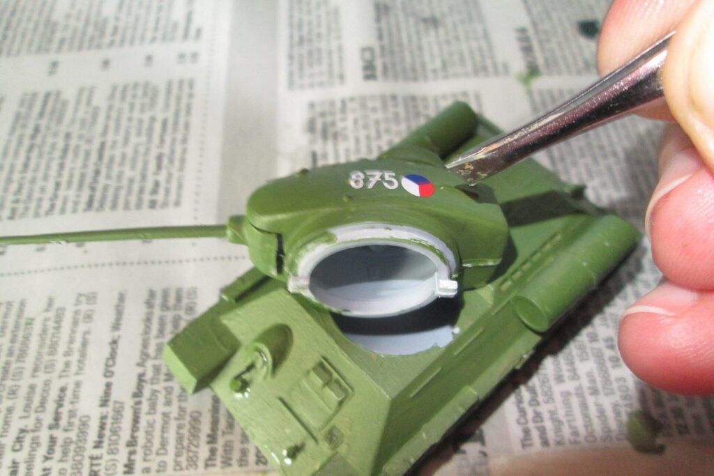 Modellbauer bringt mit einer Pinzette ein Decal auf ein grünes Panzermodell auf