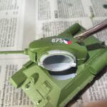 Modellbauer bringt mit einer Pinzette ein Decal auf ein grünes Panzermodell auf