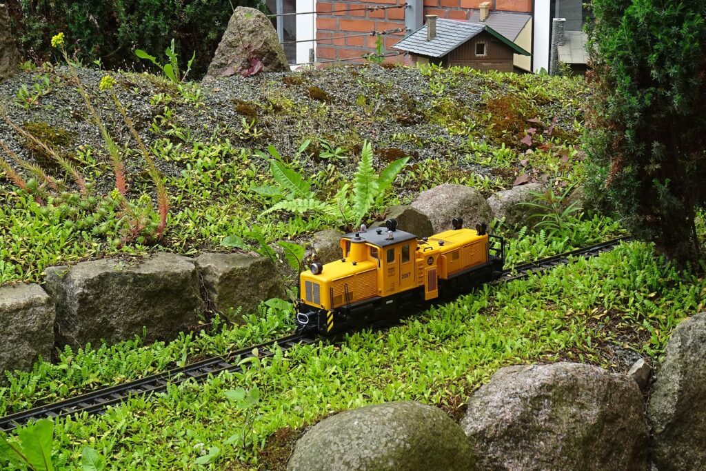 Gelbe Diesellok einer Gartenbahn fährt durch eine Gartenlandschaft