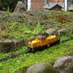 Gelbe Diesellok einer Gartenbahn fährt durch eine Gartenlandschaft