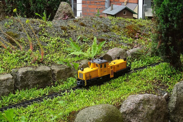 Gelbe Diesellok einer Gartenbahn fährt durch eine Gartenlandschaft