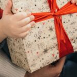Kinderhände halten ein in Geschenkpapier verpacktes Päckchen mit roter Schleife
