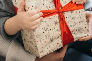 Kinderhände halten ein in Geschenkpapier verpacktes Päckchen mit roter Schleife