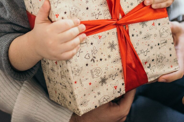 Kinderhände halten ein in Geschenkpapier verpacktes Päckchen mit roter Schleife