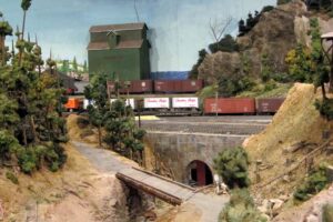 Modelleisenbahn fährt an einer gestalteten Felswand entlang in einen Tunnel