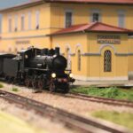 Modelleisenbahn in Spur H0 mit Dampflok vor einem gelben Bahnhofsgebäude