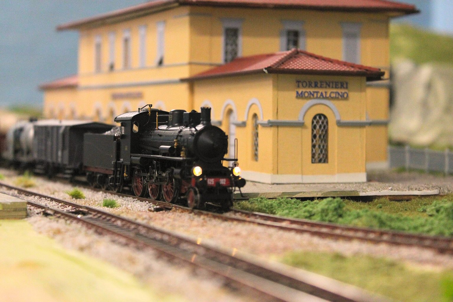 Modelleisenbahn in Spur H0 mit Dampflok vor einem gelben Bahnhofsgebäude